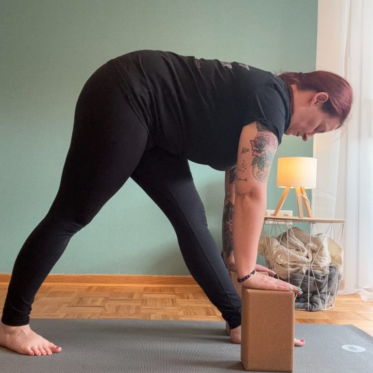 Frau in Yogahaltung - der Pyramide -  mit Block, auf einer Matte, in einem hellen Raum.