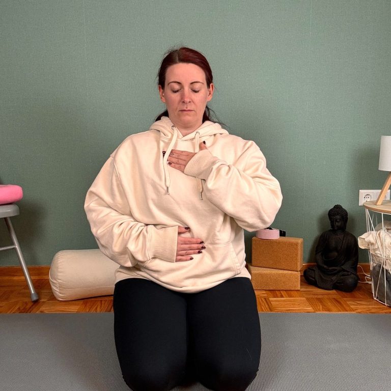 Frau in bequemer Kleidung sitzt im Schneidersitz und übt Atemtechniken.