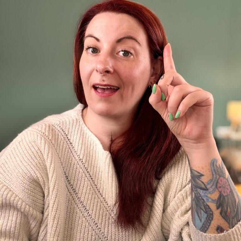 Meike zeigt mit Finger nach oben. Es sieht aus, als ob sie "Aha!" sagt. Sie trägt einen hellen Pullover.