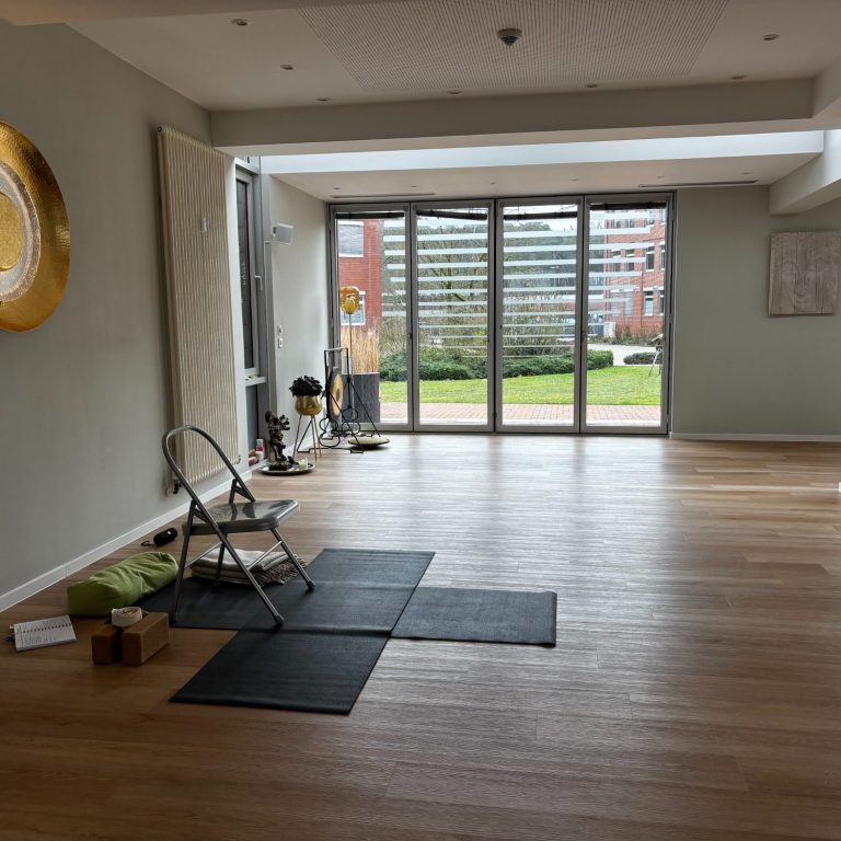 Heller Raum mit Holzfußboden, Stuhl und Blick auf einen Garten durch große Fenster.